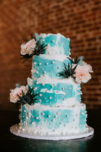 blue wedding cake adorned with pink flowers and edible pearls