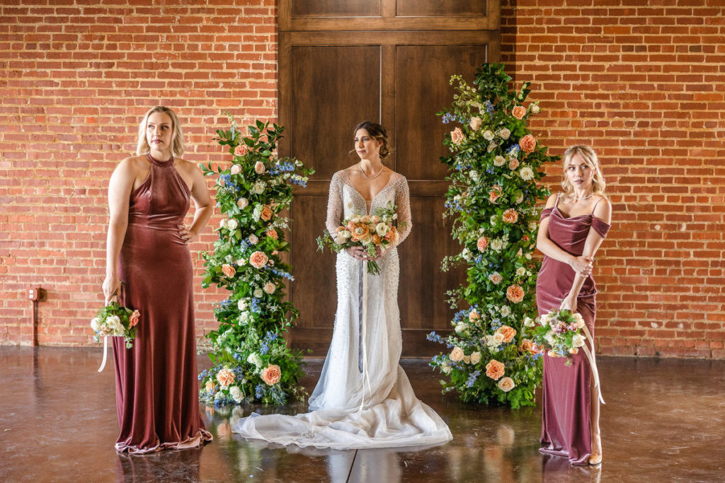 bride standing between bridesmaids and flower pillars